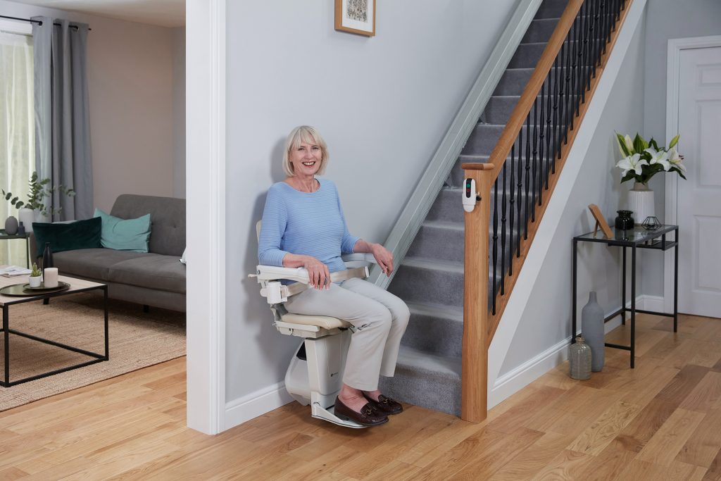 Woman smiling at the bottom of her staircase sitting on her stairlift